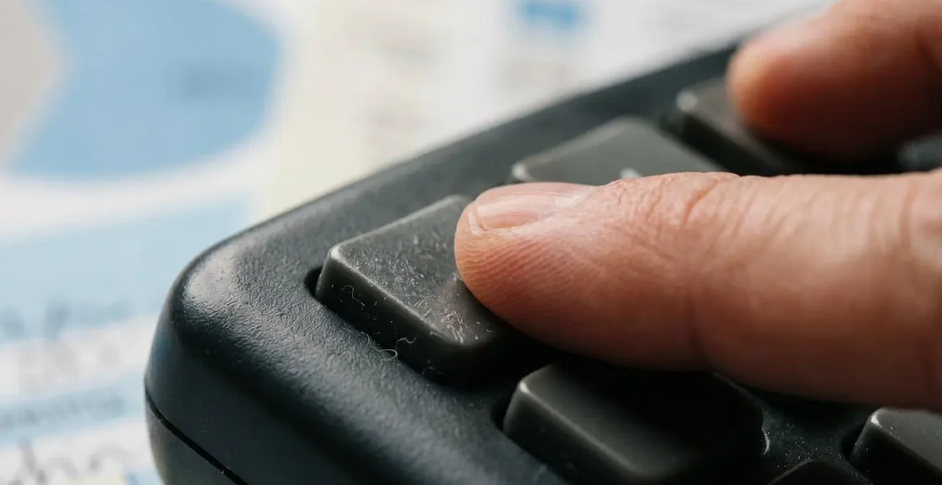 Gros plan sur une main utilisant une calculatrice avec des papiers médicaux flous en arrière-plan